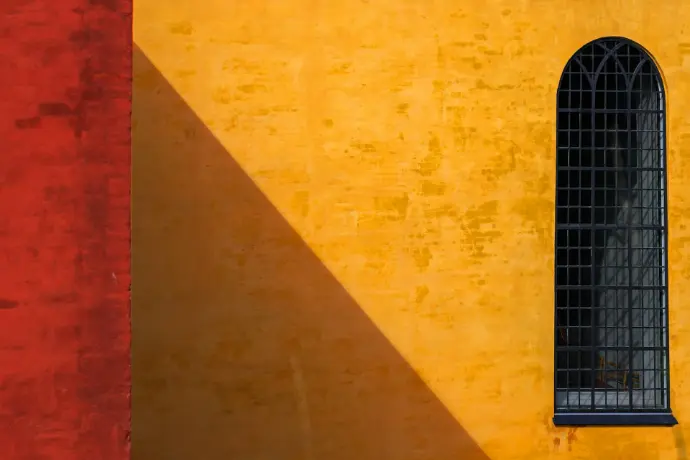 A yellow building with a black window and a red wall